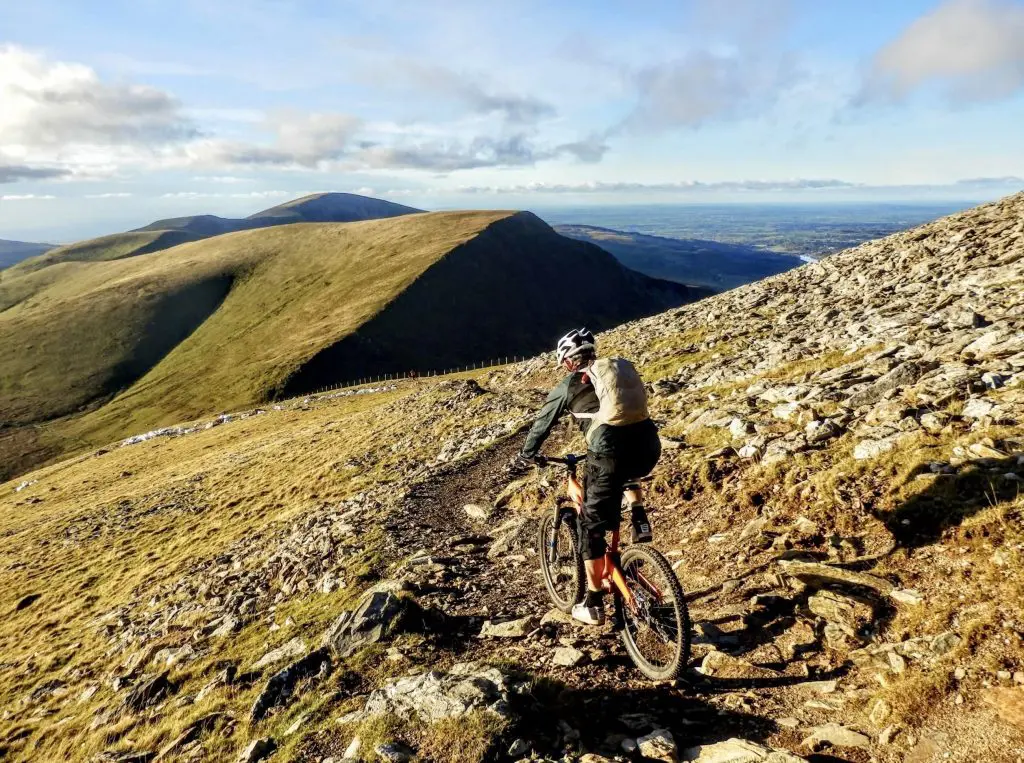 Mountain biker riding a red-and-black bicycle along a rugged rocky trail across scenic mountain slopes. - Mountain Biking on Yr Wyddfa (Snowdon) North Wales