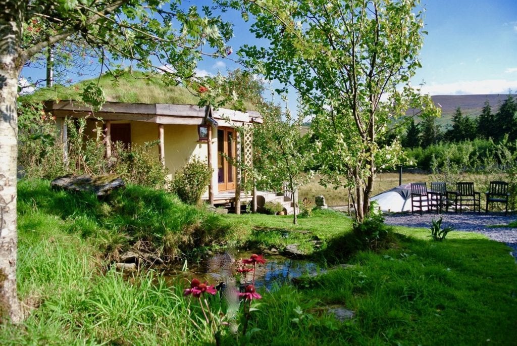 Straw bale roundhouse and yurt from behind pond at Ty Mam Mawr eco retreat centre